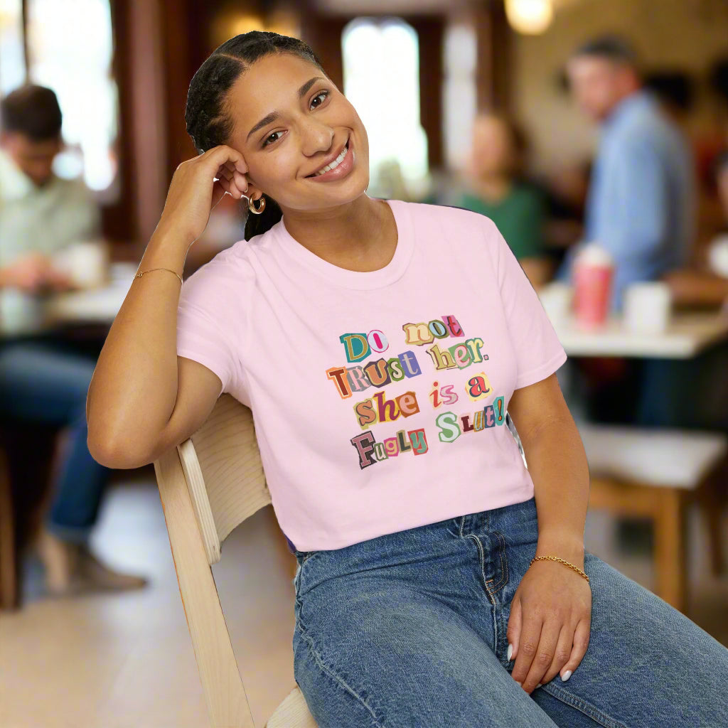 Person wearing a pink t-shirt with colorful text, sitting on a chair against a white background
