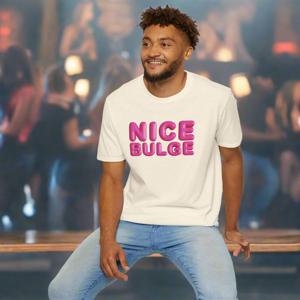 Man wearing a cream t-shirt with 'NICE BULGE' in pink text, sitting on a white stool against a white background.