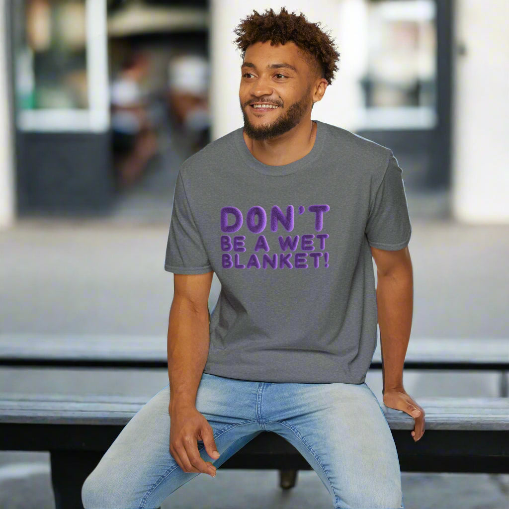 Man wearing a gray t-shirt with purple text sitting on a white stool against a white background
