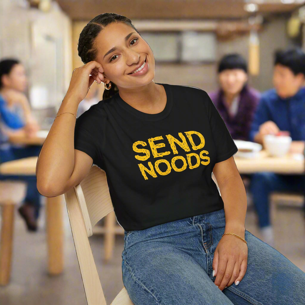 Person wearing a black t-shirt with 'SEND NOODS' in yellow text, sitting on a chair.