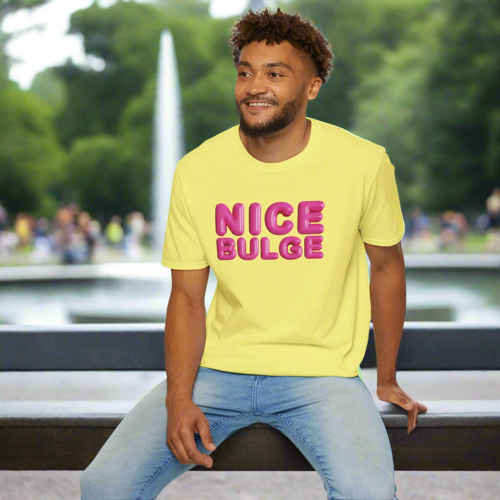 Man wearing a yellow t-shirt with 'NICE BULGE' in pink text, sitting on a white stool against a white background.
