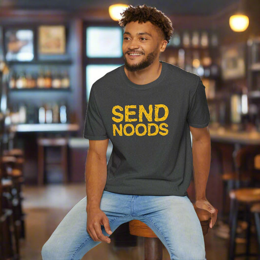 Man wearing a dark gray t-shirt with 'SEND NOODS' in yellow text, sitting on a white stool against a white background.